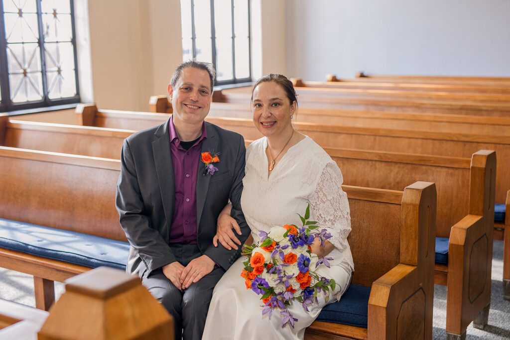 Wes and Rachele sit together on the benches inside the courtroom with the beautiful afternoon sunlight shining in through the windows.