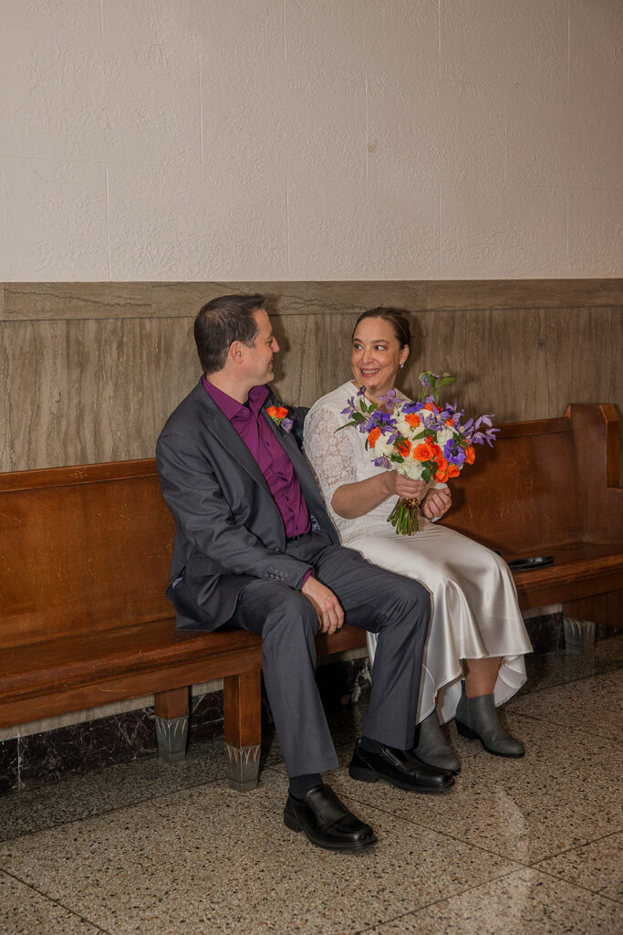 Wes and Rachele sit together on the long wooden bench in the hallway outside the Justice of the Peace office, waiting to be called into the courtroom.