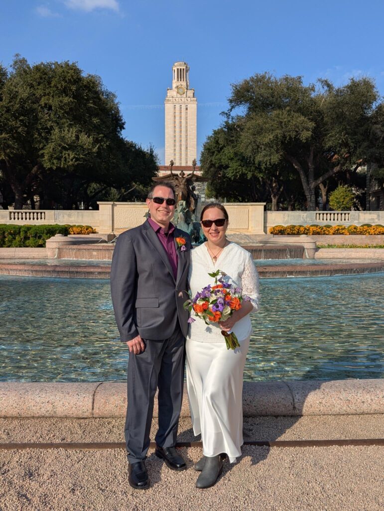 Wes and Rachele in their wedding clothes standing in front of Littlefield Fountain with the UT Tower in the background on their very sunny wedding day