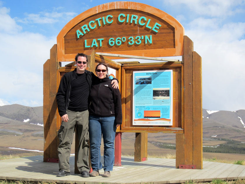 Wes and Rachele standing at the marker for the Arctic Circle on the Dempster highway in Yukon